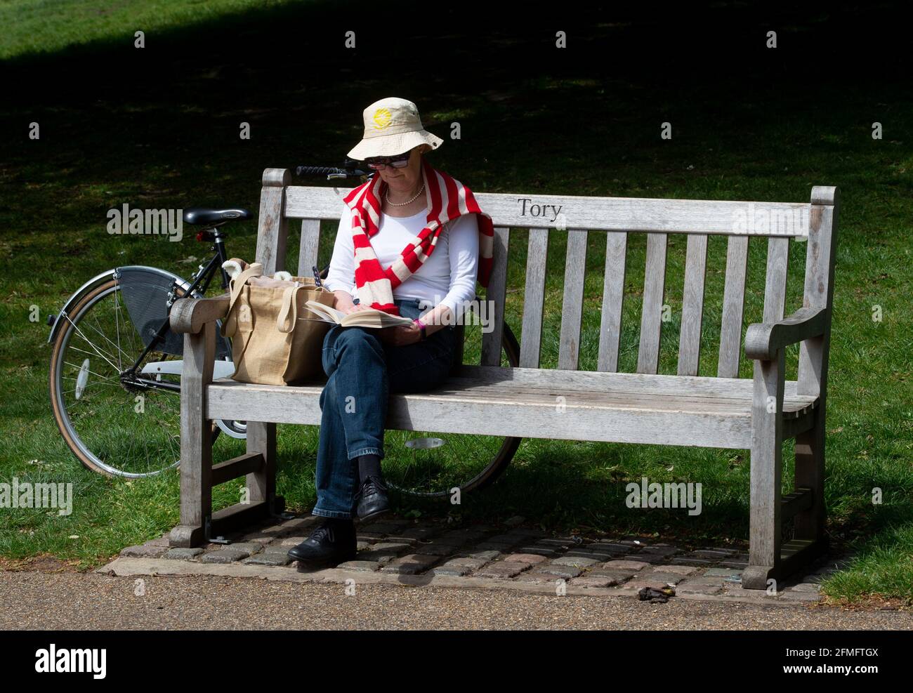 London, Großbritannien. Mai 2021. Eine Frau sitzt auf einer Bank, auf der das Wort „Tory“ steht. Die Menschen genießen das schöne Wetter im Hyde Park, London, da die Temperaturen auf 19 Grad Celsius eingestellt sind. Dies kommt nach dem kältesten April seit mehr als 50 Jahren. Kredit: Mark Thomas/Alamy Live Nachrichten Stockfoto