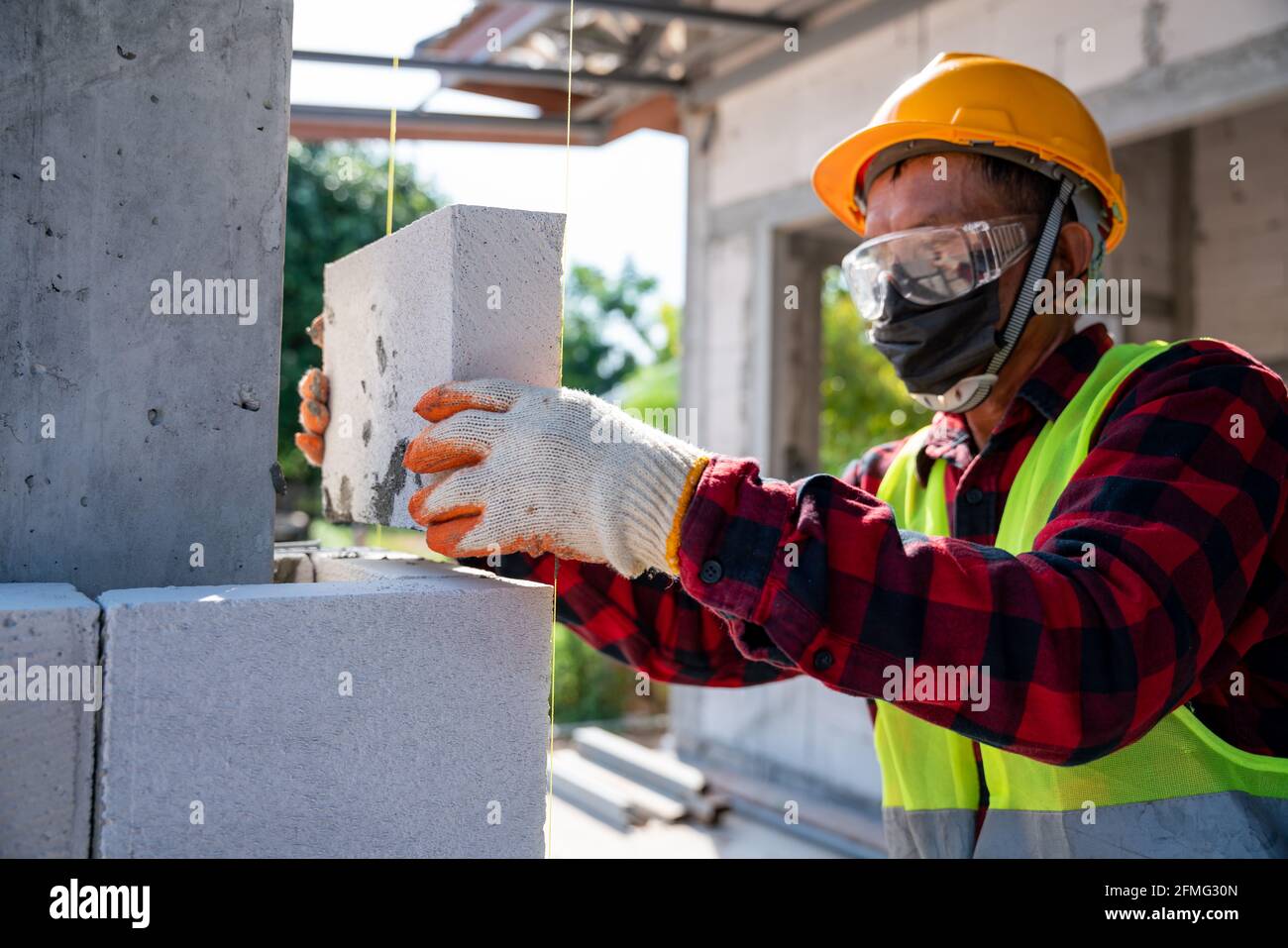 Maurerbauer, der mit autoklavierten, belüftelten Betonblöcken arbeitet. Mauerwerk, Montage von Ziegeln auf der Baustelle Stockfoto