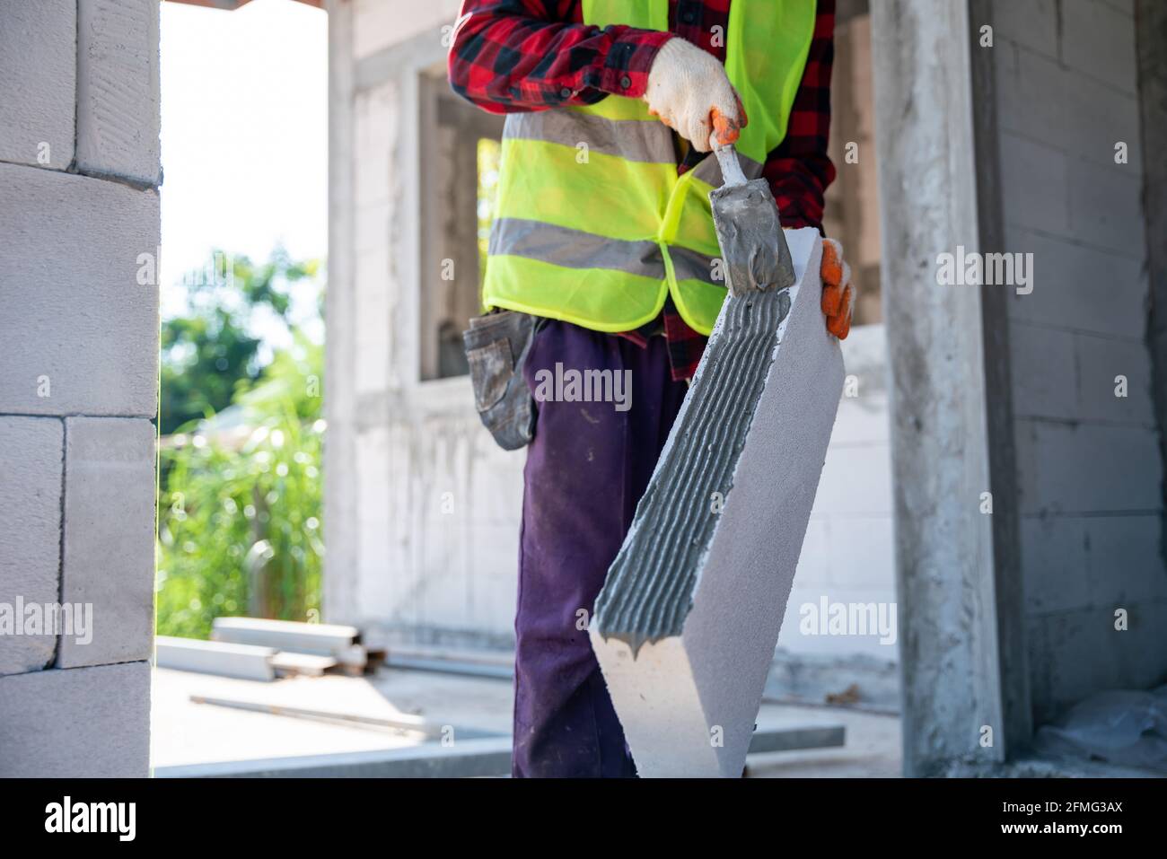 Nahaufnahme von Maurerbauer, der autoklaviert und mit Pflaster-Betonklötzen belüftet arbeitet. Mauerwerk, Installation von Ziegeln an unfertigen Haus c Stockfoto