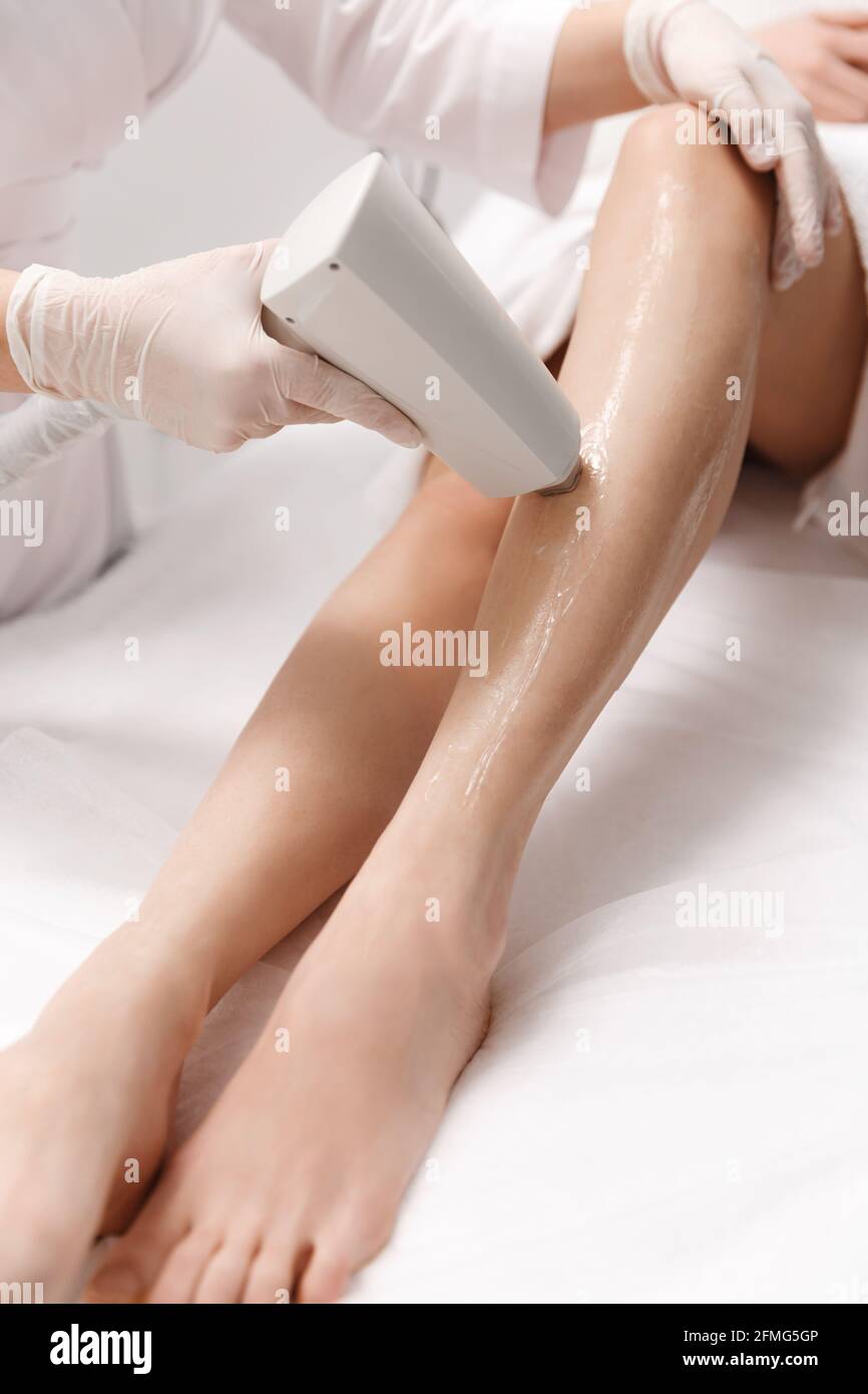 Nahaufnahme der Beine Laser-Haarentfernung Verfahren von Schönheitsklinik Spezialisten in Handschuhen durchgeführt. Kosmetikerin betäubt die Haut vor der Anwendung mit kühlenden Gel Stockfoto