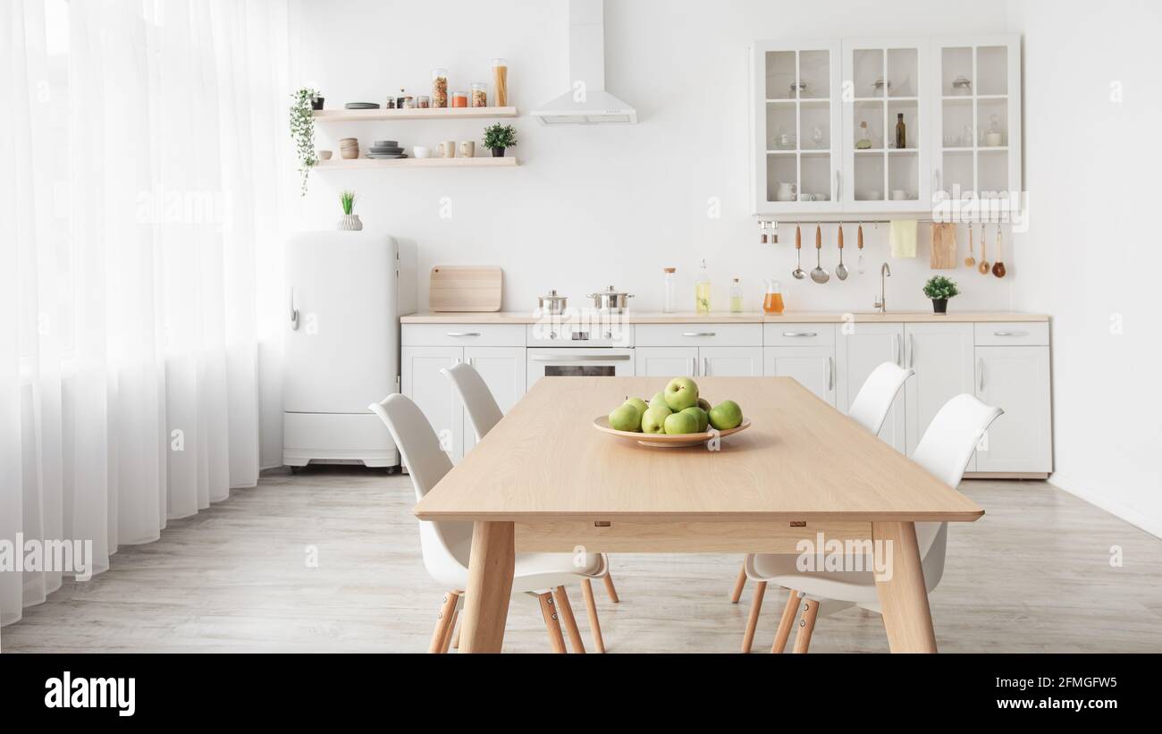 Moderne, minimalistische Einrichtung von Küche und Esszimmer. Weiße Möbel mit Utensilien und Esstisch mit Stühlen Stockfoto