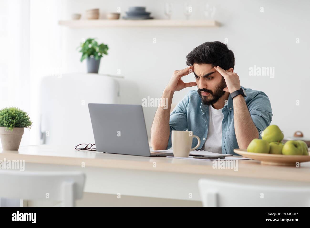 Gestresste arabische männliche Unternehmer Probleme bei der Arbeit, sitzen aufgeregt mit Laptop-Computer am Küchentisch Stockfoto