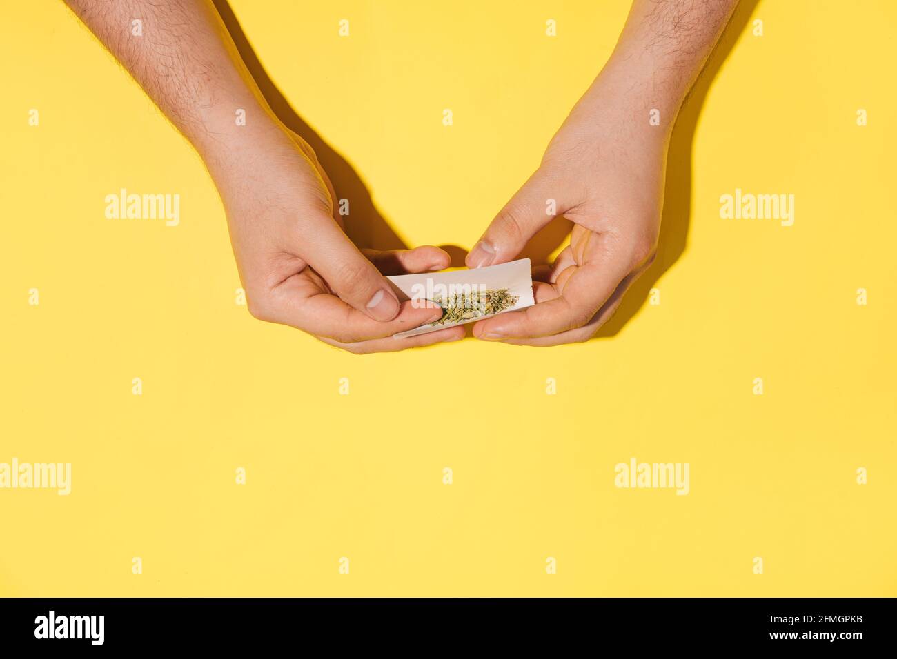 Die Hände des Mannes Rollen trockenen Cannabis oder Kräuter Rauch auf Hipster gelben Hintergrund. Flach liegend. Stockfoto