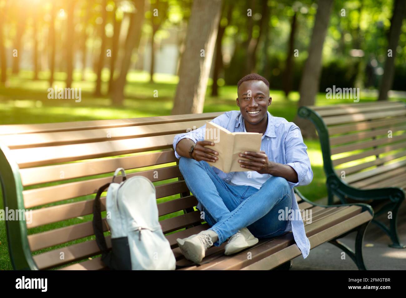 Funky afroamerikanischen Kerl liest faszinierende Buch auf Bank im Stadtpark, leeren Raum Stockfoto