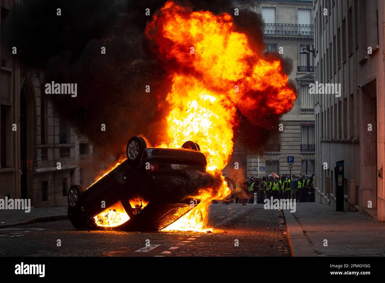Ein Auto brennt in Flammen, während Demonstranten von einem aus zuschauen Entfernung auf einer Straße in der Nähe des Triumphbogens während Der vierte Samstag der nationalen Proteste der „y Stockfoto