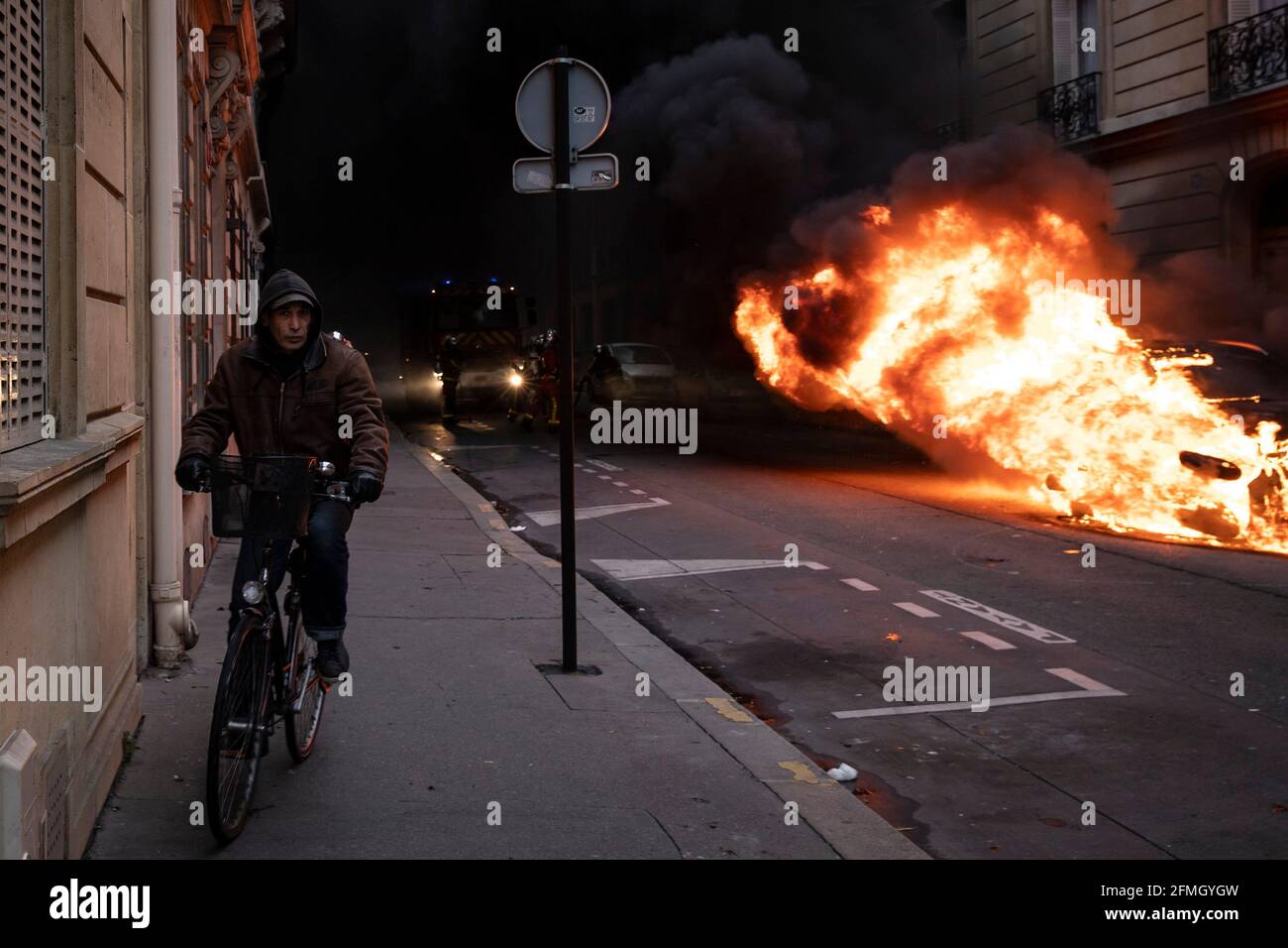 Ein Mann fährt an einem brennenden Fahrzeug vorbei und fährt mit dem Roller weiter Eine Straße in der Nähe des Triumphbogens während der vierten Samstag der nationalen Proteste der „gelben Weste“ Stockfoto