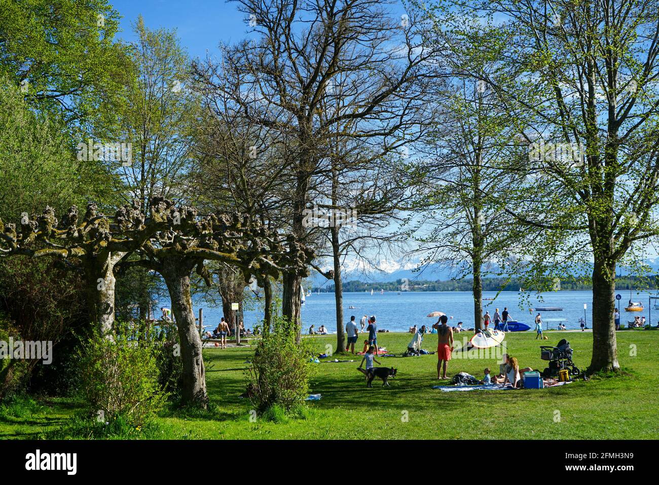 Zahlreiche Menschen genießen ihre Freizeit im Sonnenschein am Ufer eines Sees. Stockfoto