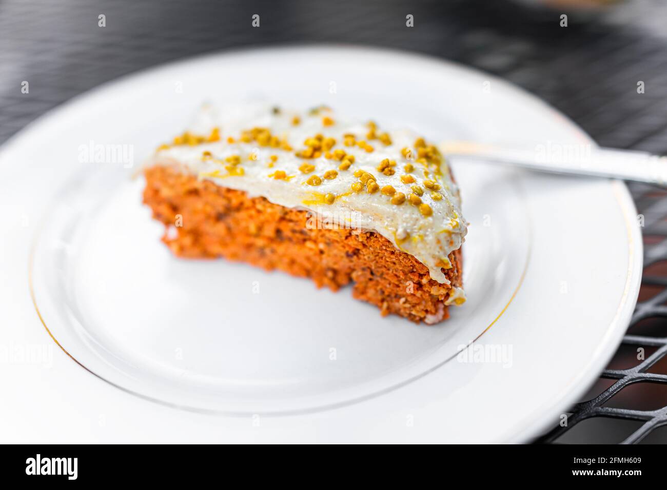 Karottenkuchen Stückchen auf weißem Teller süß roh Dessert Mit Frischkäse-Zuckerguss und orangefarbener Textur mit Bienenpollen Darauf gestreut Stockfoto
