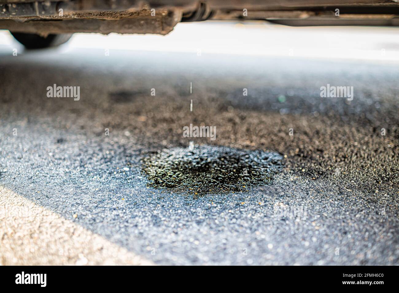 Geparktes Auto auf der Straße mit Makro-Nahaufnahme des Fahrzeugs Undichter Kraftstoff mit Pfütze, der den Asphalt beschädigt Stockfoto