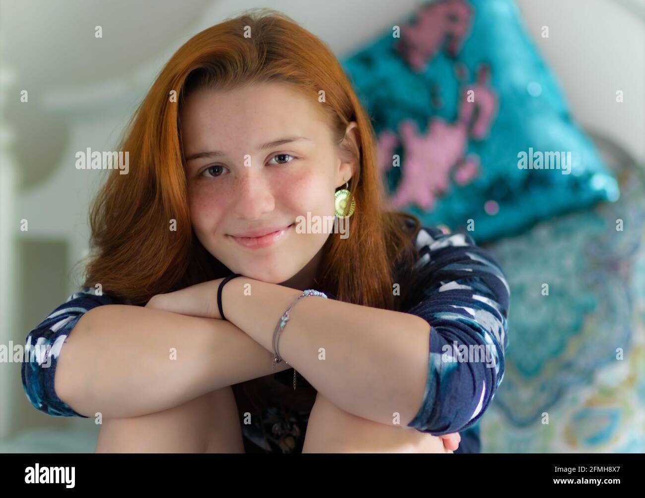 Eine hübsche High School Mädchen oder weibliche College-Studentin mit Rote Haare im Schlafzimmer oder Schlafsaal mit einem selbstbewussten Lächeln Und den Kopf auf den Händen auf den Knien ruhen Stockfoto