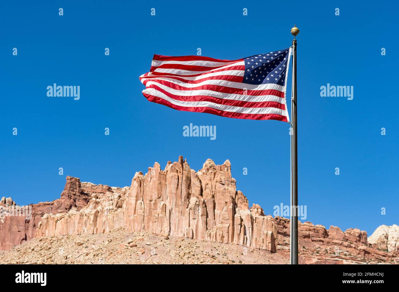 American Flag fliegt im Wind an einem sonnigen Tag, ikonische rote Sandsteinfelsen bilden DIE BURG in der Ferne, Capitol Reef National Park, Utah Stockfoto