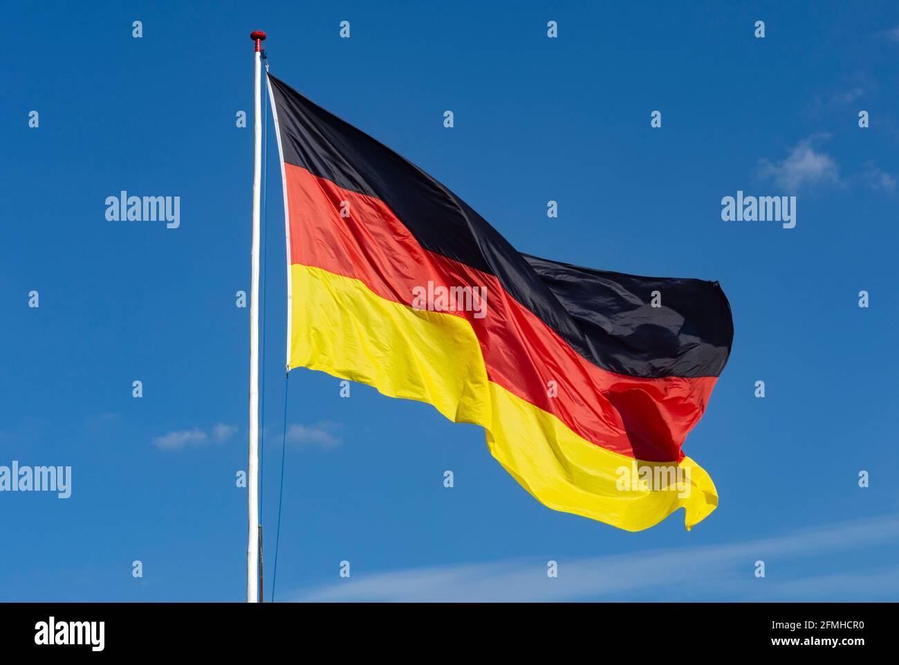 Große deutsche Flagge fliegend von handgefertigtem Holzfahnenmast mit Weiße Farbe mit einem wolkenlosen blauen Himmel dahinter Stockfoto