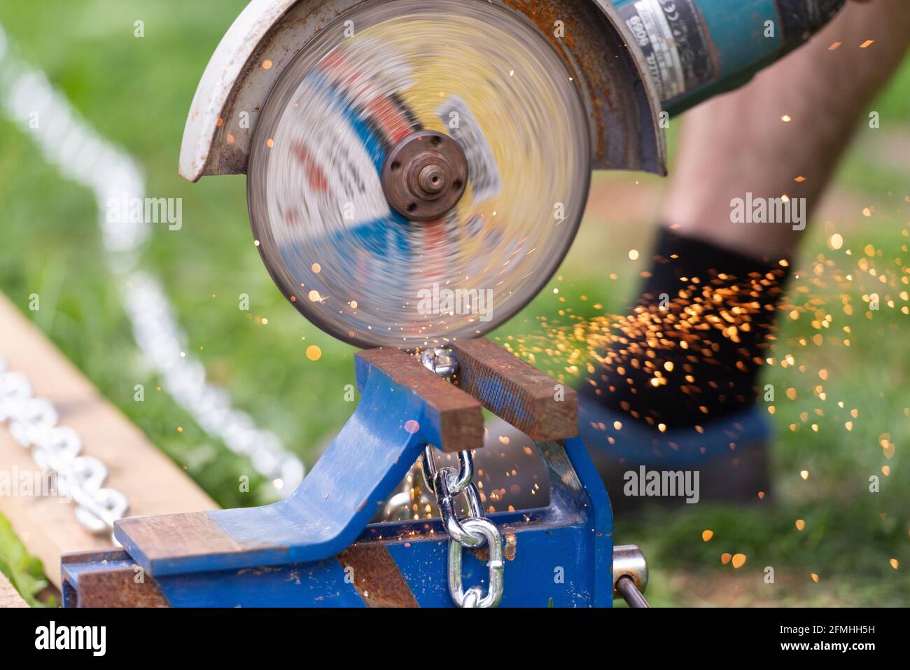 Ein Arbeiter sägt eine Kette mit einem Schleifer. Am Schraubstock ist eine Chromkette befestigt, die in Stücke geschnitten wird. Funken durch Arbeiten mit Metall. Stockfoto