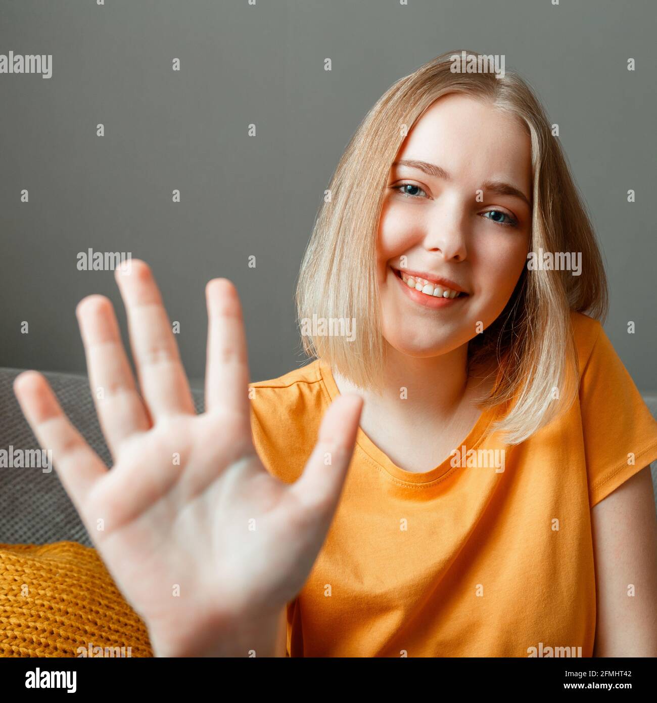 Glückliche Frau Porträt Welle von Hand Gruß Web Kamera Ansicht. Junge, schöne Frau, die mit einem Videoanruf auf dem Sofa im Wohnzimmer spricht Stockfoto