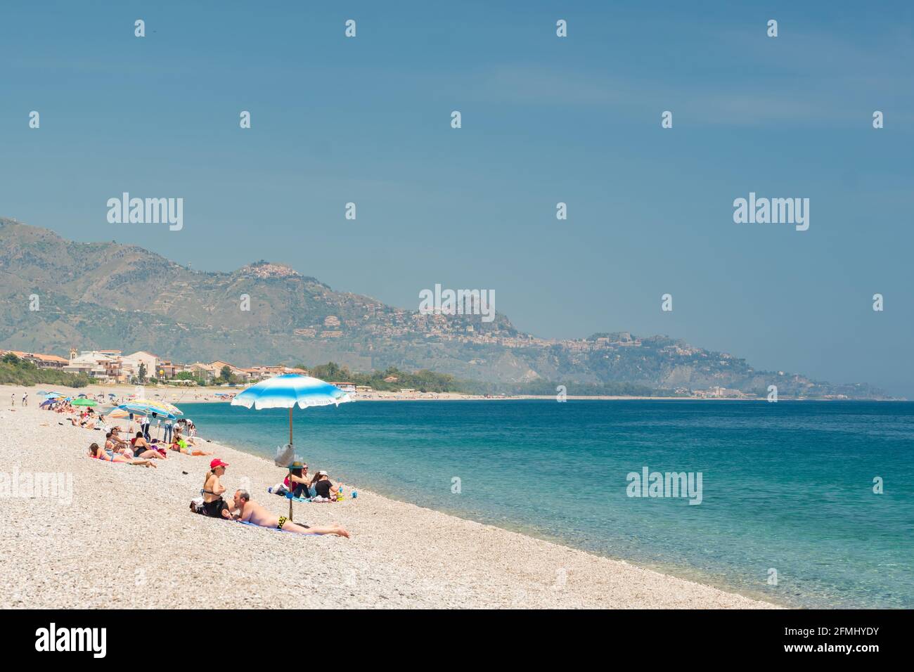 Nicht identifizierte Menschen am Strand in Giardini Naxos mit Taormina Stadt im Hintergrund, Sizilien Stockfoto