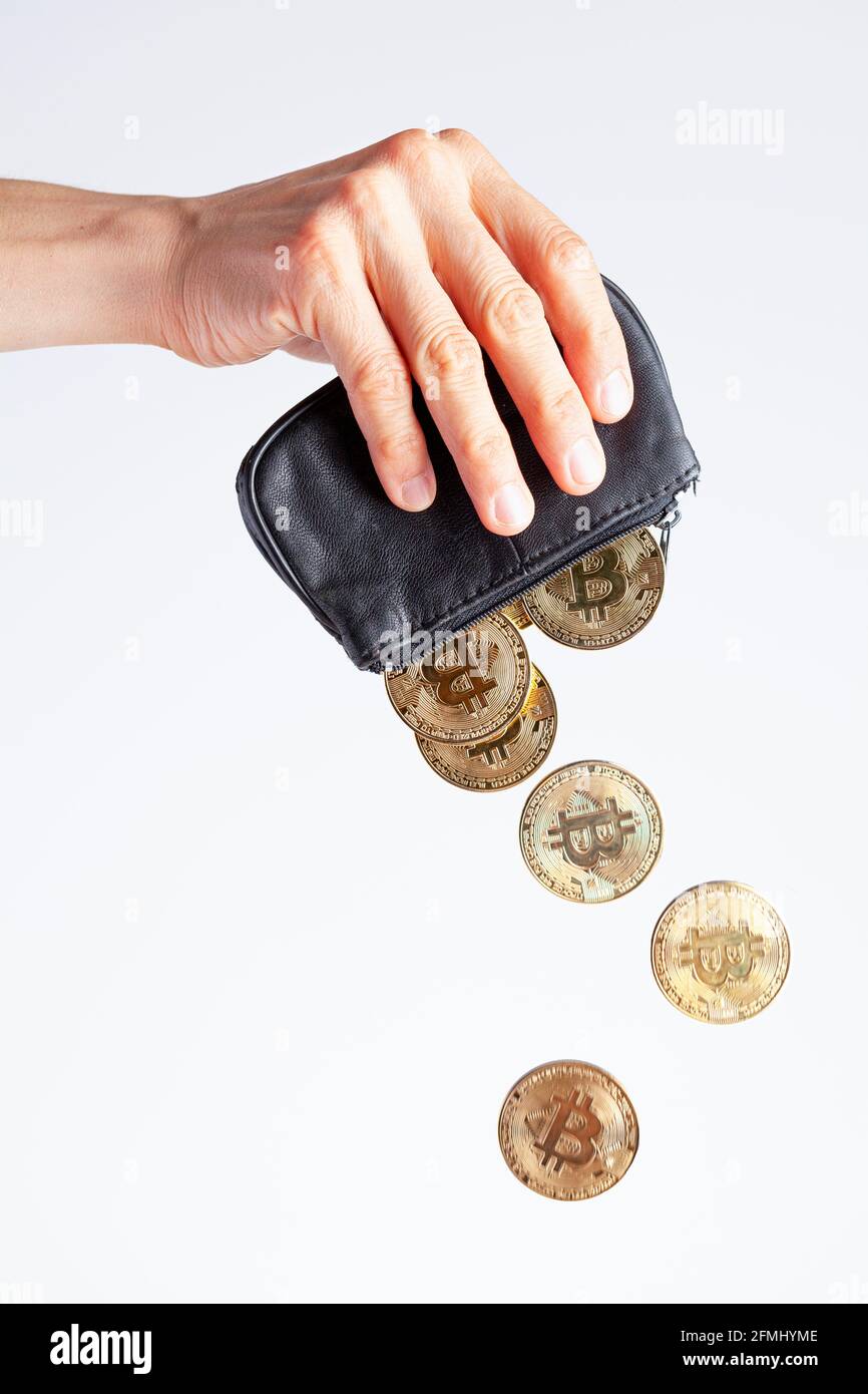 Isoliertes Bild einer kaukasischen Frau, die eine schwarze Handtasche vor hellweißem Hintergrund hält. Bitcoin-Münzen fallen vom Geldbeutel, als sie leert. Weinen Stockfoto