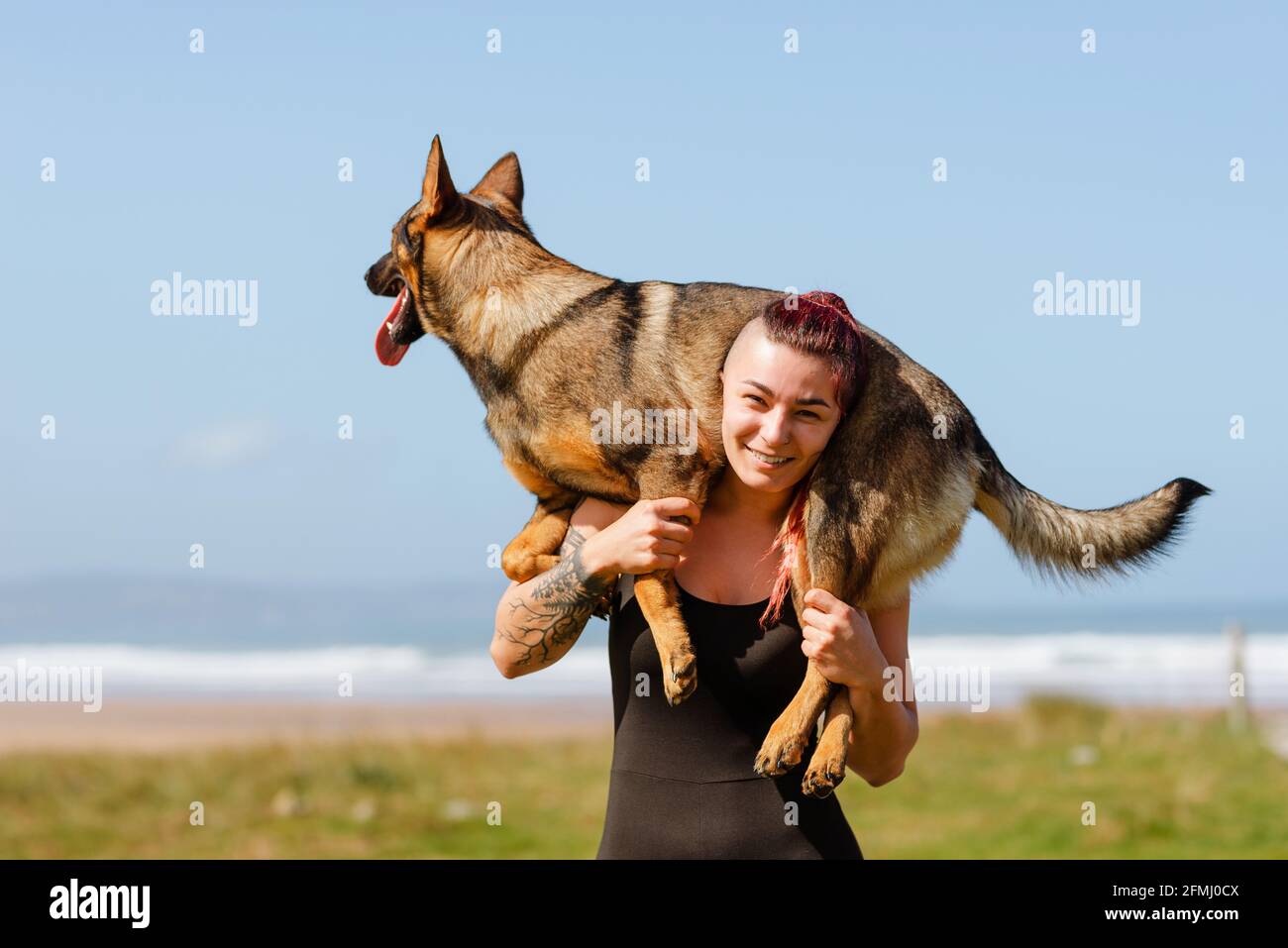 Tätowierte weibliche Athletin mit niedlichen reinrassigen Hund auf den Schultern suchen An sonnigen Tagen vor der Kamera Stockfoto