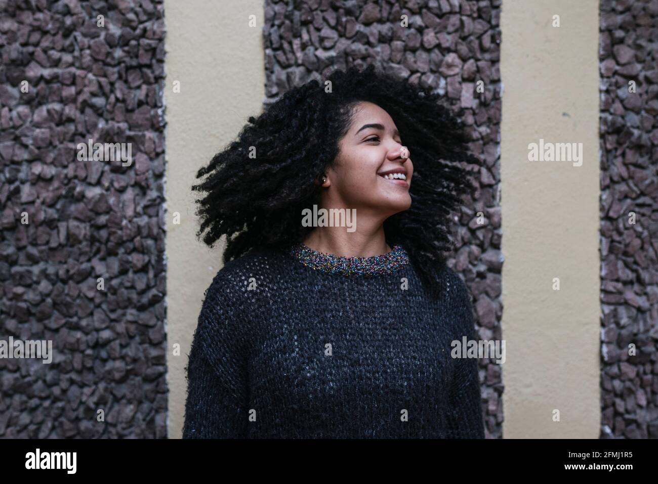 Inhalt Ethnisches Weibchen mit Afro-Frisur, das im Stehen Haare wirft Auf der Straße und lächelnd Stockfoto