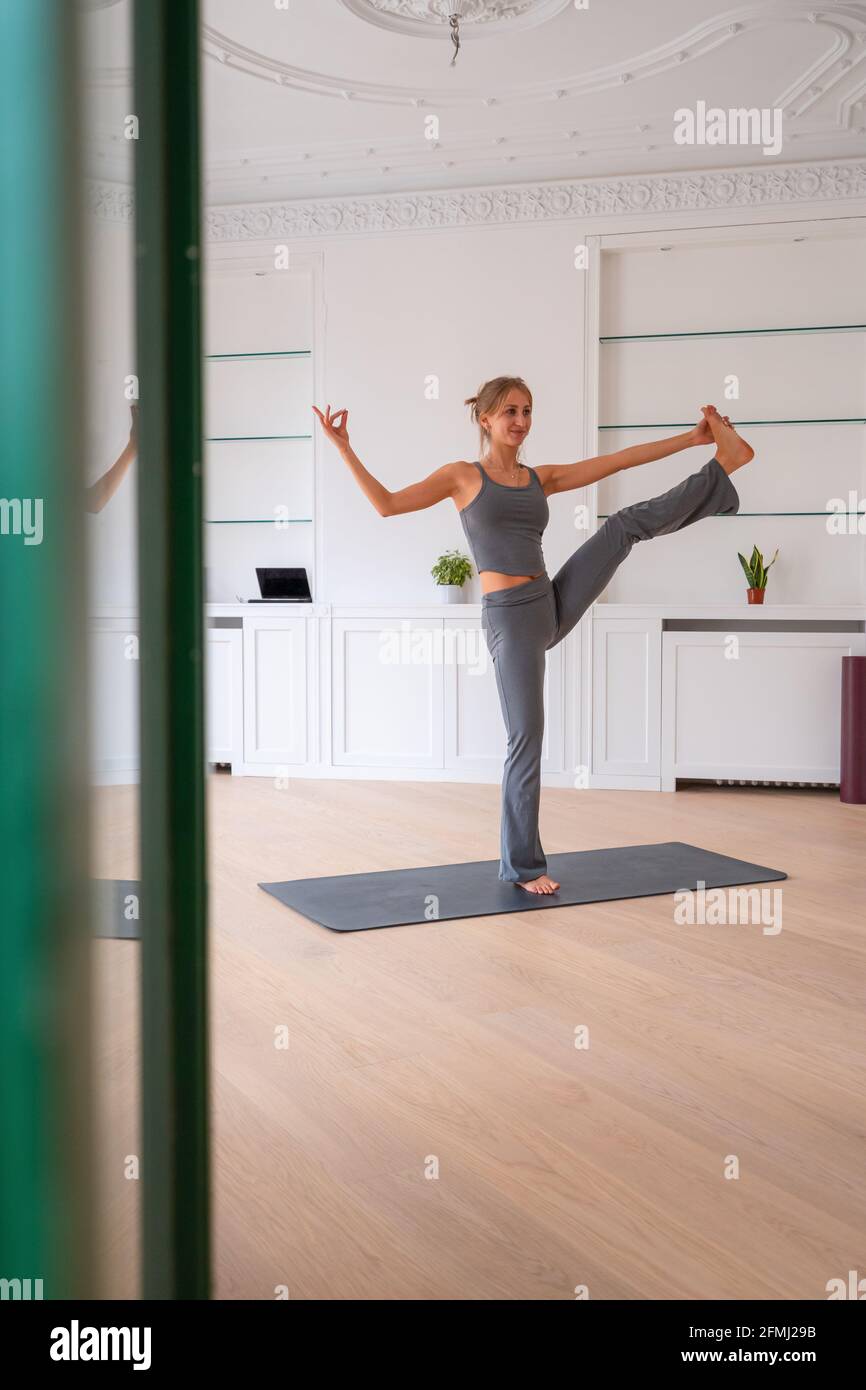 Passen Sie glückliche weibliche Stretching-Beine in Extended Hand zu Big Zehenhaltung beim Stehen und Balancieren auf der Matte zu Hause Stockfoto