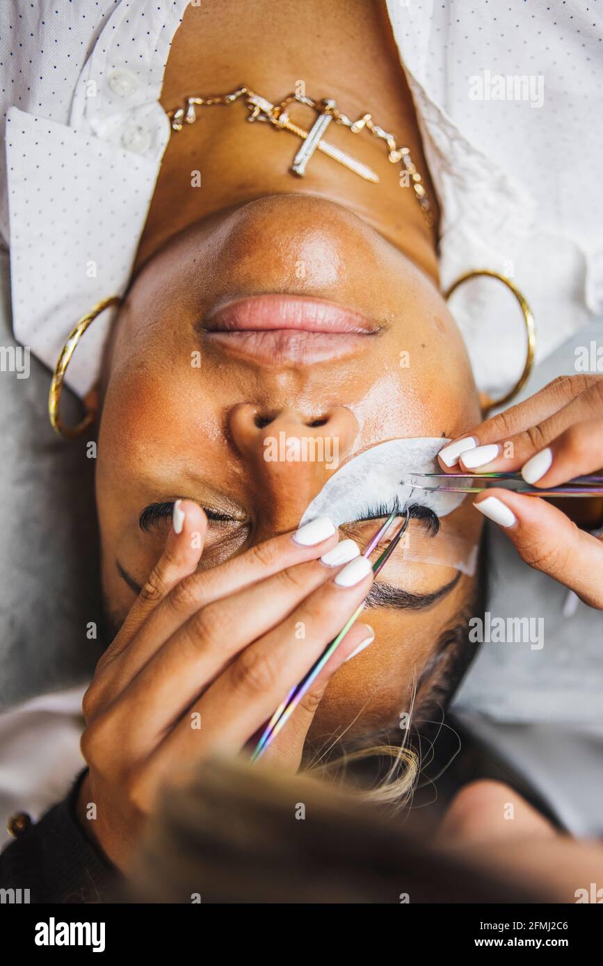 Hoher Winkel der Ernte unkenntlich Kosmetologe mit Pinzette Anwendung gefälschte Wimpern zur Erweiterung auf das Auge des ethnischen Kunden im Salon Stockfoto