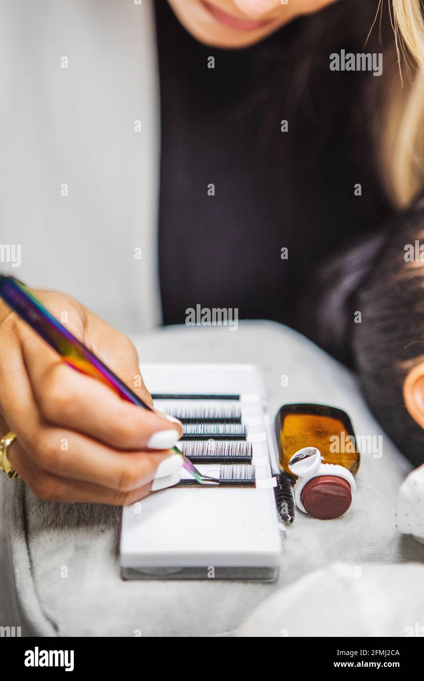 Crop anonyme Beauty-Techniker mit Pinzette nehmen Wimpern für die Verlängerung gegen ethnische Frau während der Kosmetologie Verfahren Stockfoto