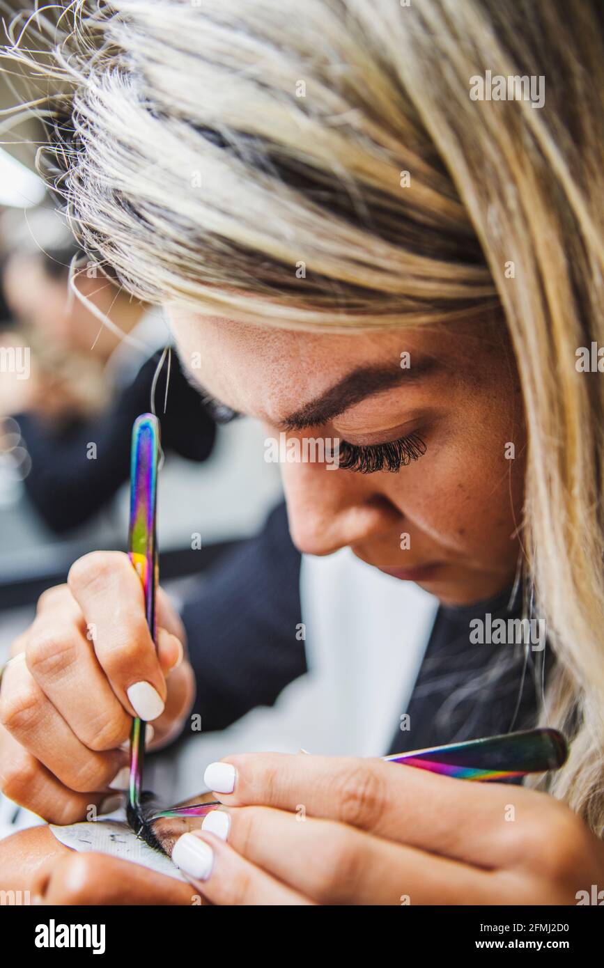 Weibliche Schönheitsmeisterin mit einer Pinzette, die gefälschte Wimpern auf das Gesicht aufgetragen hat Von beschnitten nicht erkennbaren ethnischen Kunden im Salon Stockfoto