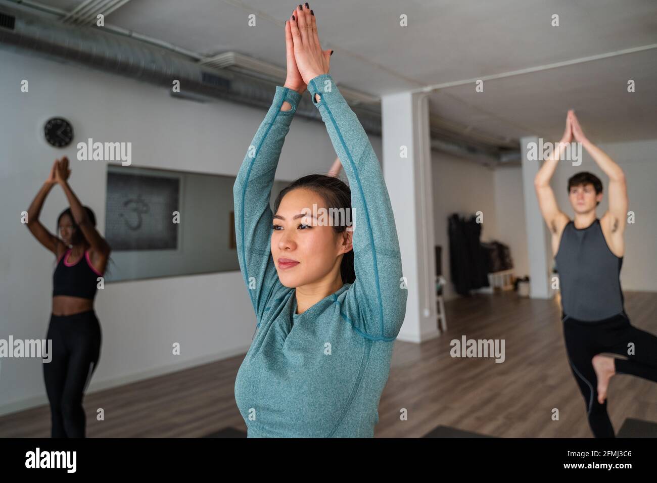 Heitere Hündin in Sportswear, die in Bergpose mit Ausstreckung steht Arme beim Yoga in der Gruppe im Studio Stockfoto