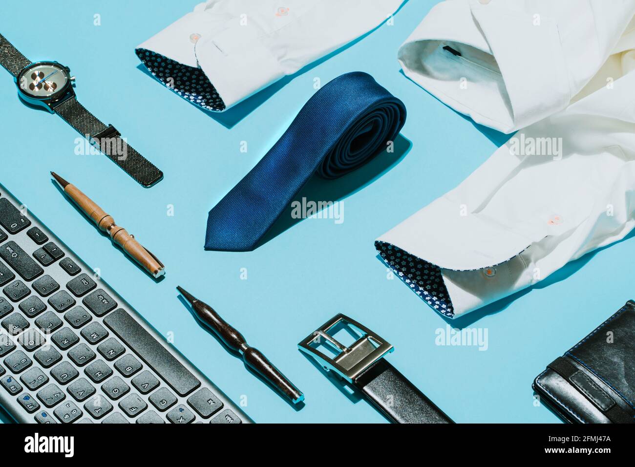 Von oben elegantes weißes Hemd mit blauer Seidenkrawatte Und Armbanduhr auf Tisch mit Ledergürtel und kreativ angeordnet Stifte in der Nähe der Computertastatur Stockfoto