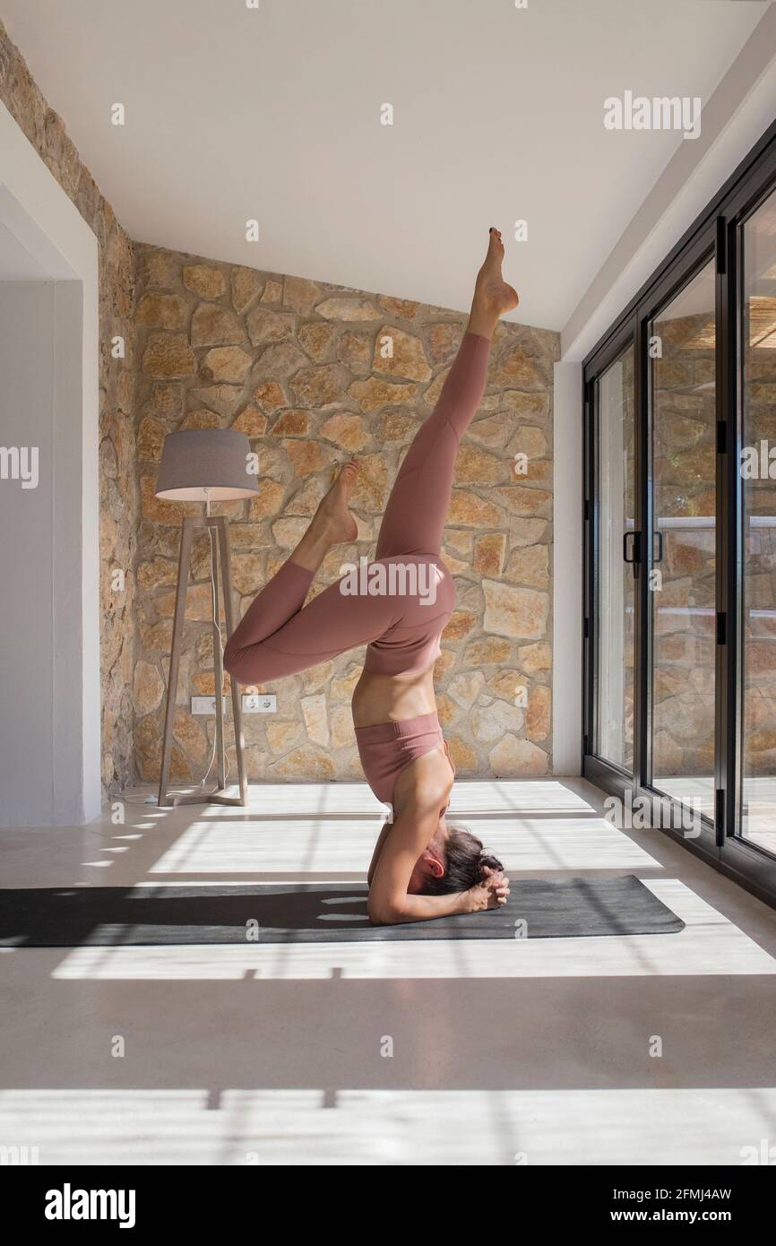 Seitenansicht einer anonymen Frau in Sportkleidung, die auf dem Kopf steht Mit erhöhten Beinen, während Sie zu Hause Yoga praktizieren Stockfoto