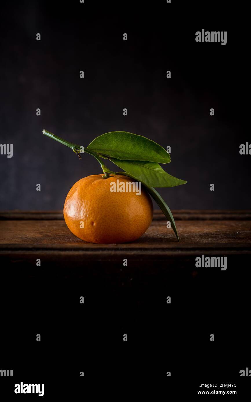 Ganze ungeschälte Mandarine mit Pediküre und welligen Blättern mit spitz Kanten auf Holzoberfläche Stockfoto