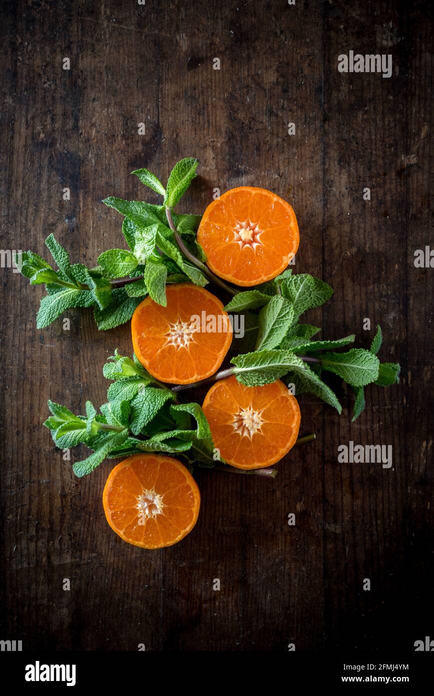 Ansicht von oben auf frische Mandarinenhälften mit saftigem Fruchtfleisch darunter Minze Laub auf braunem Hintergrund Stockfoto