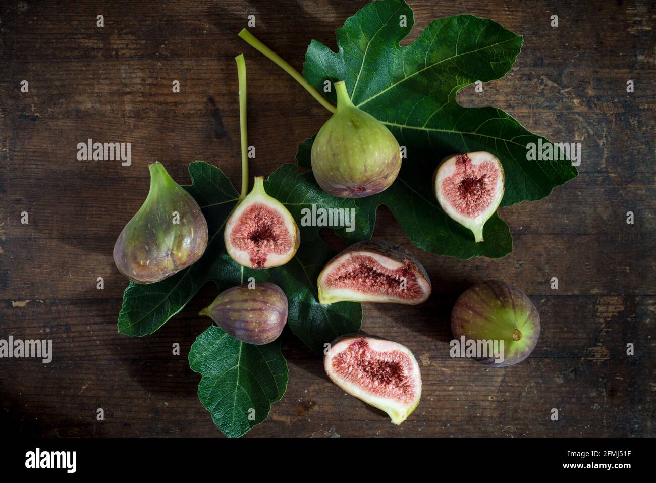 Draufsicht auf ganze und geschnittene Feigen mit saftigem Fruchtfleisch Auf grünem Laub mit Adern auf hölzerner Oberfläche Stockfoto