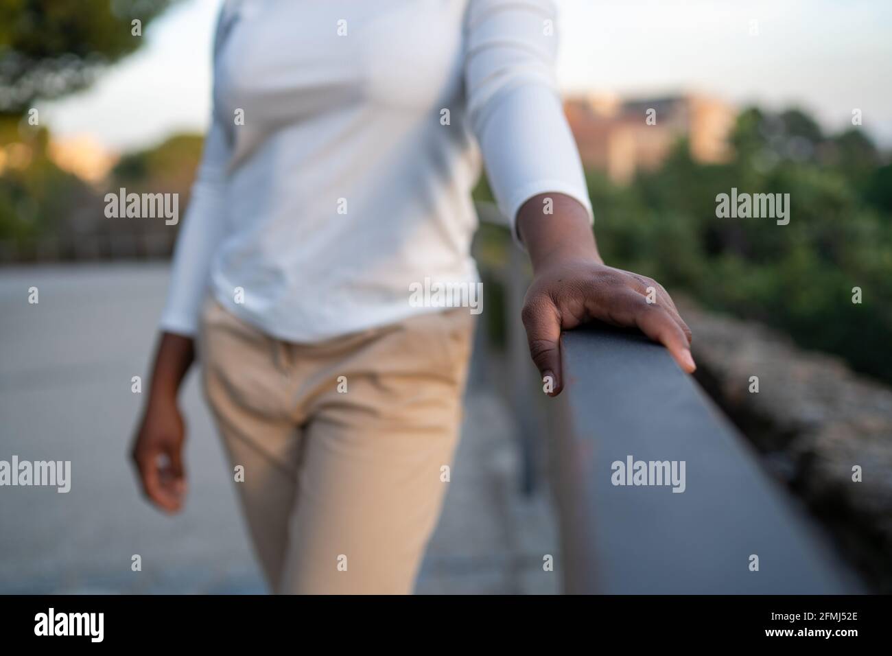 Crop afroamerikanische Frau in legerer Kleidung in der Nähe von Zaun stehen Im üppigen Stadtpark am Sommertag und Blick weg Stockfoto