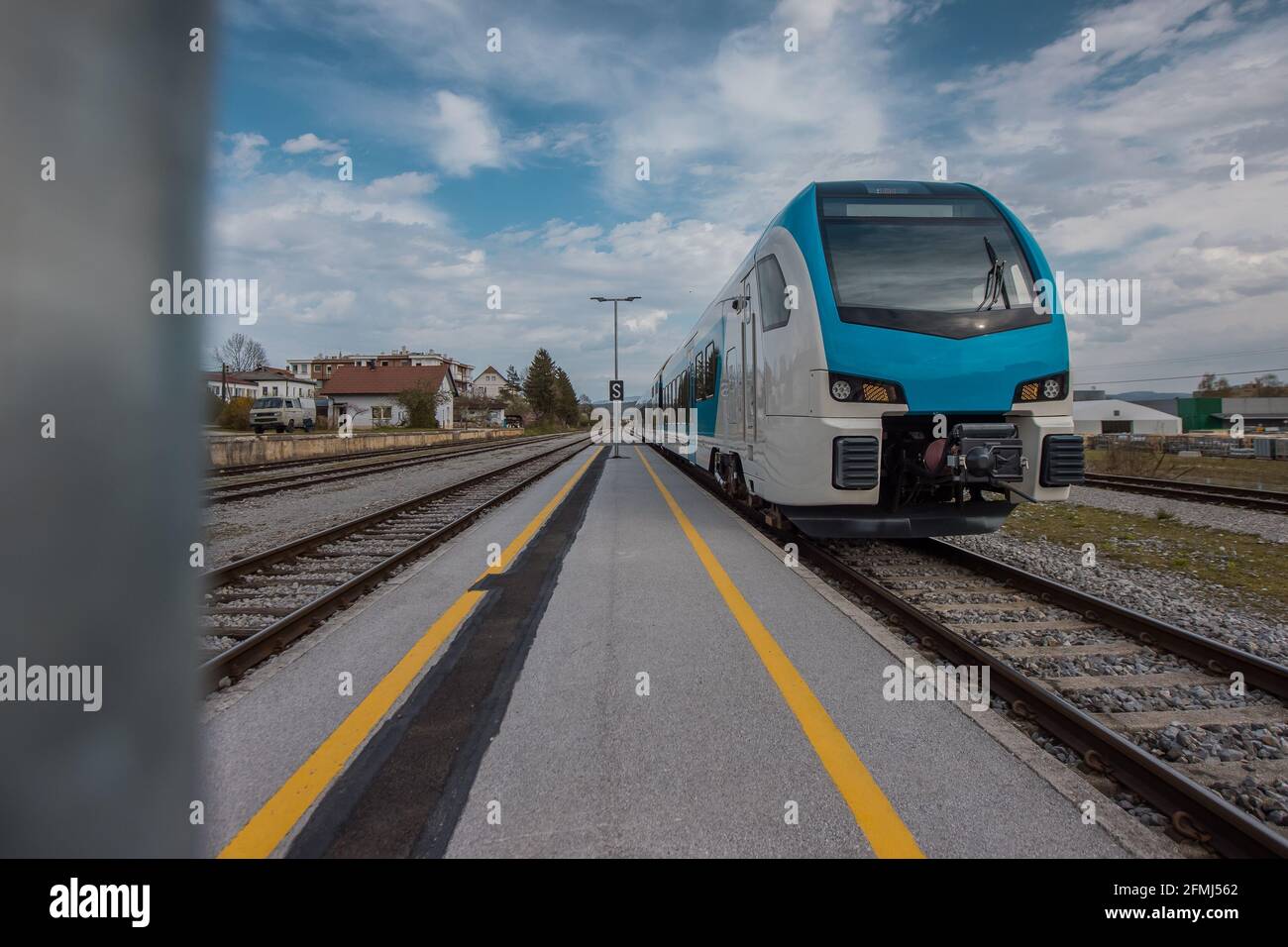 Moderner weißer und blauer Personenzug, der zu einer Haltestelle im Bahnhof vor einem modernen Wohnungs- oder Wohnviertel kommt. Stockfoto