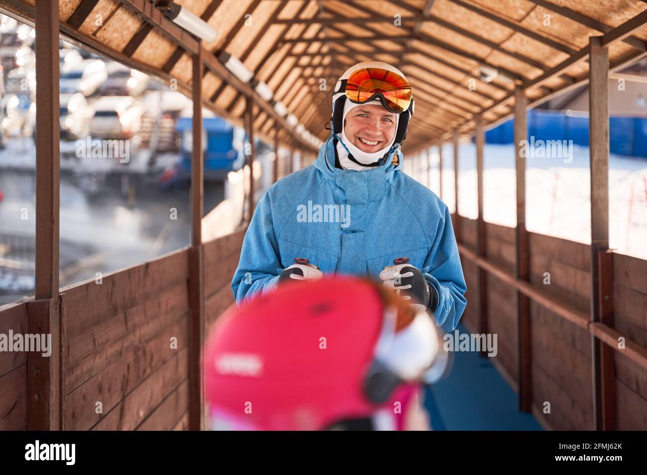Fröhlicher Vater mit Skihelm und warmer Sportswear im Stehen Sonniger Outdoor-Sportclub und mit einem Lächeln auf die Kamera schauen Stockfoto