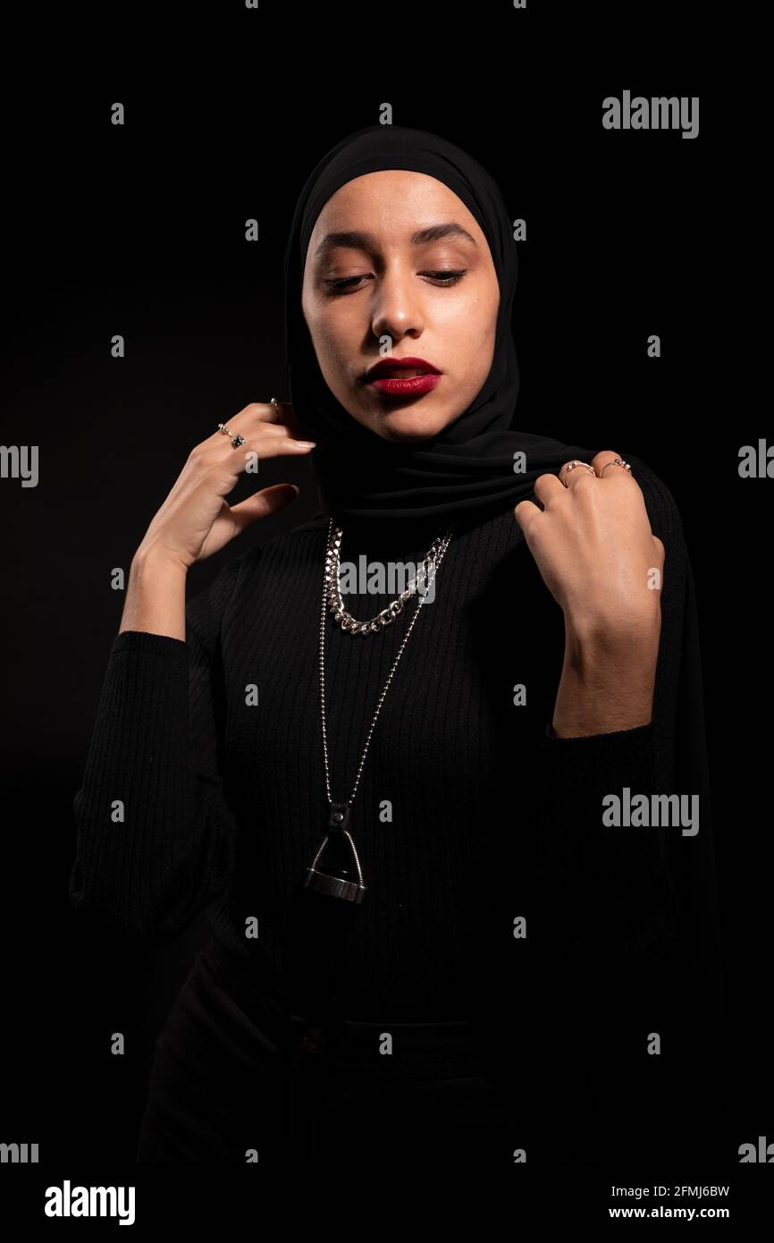 Attraktive junge islamische Frau in schwarzem Outfit und Hijab sanft Nach unten schauen Stockfoto
