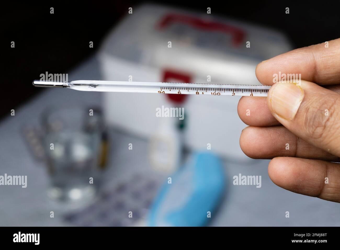 Selektiver Fokus auf ein analoges Thermometer, das in menschlicher Hand gehalten wird Mit Medizin auf Hintergrund Stockfoto