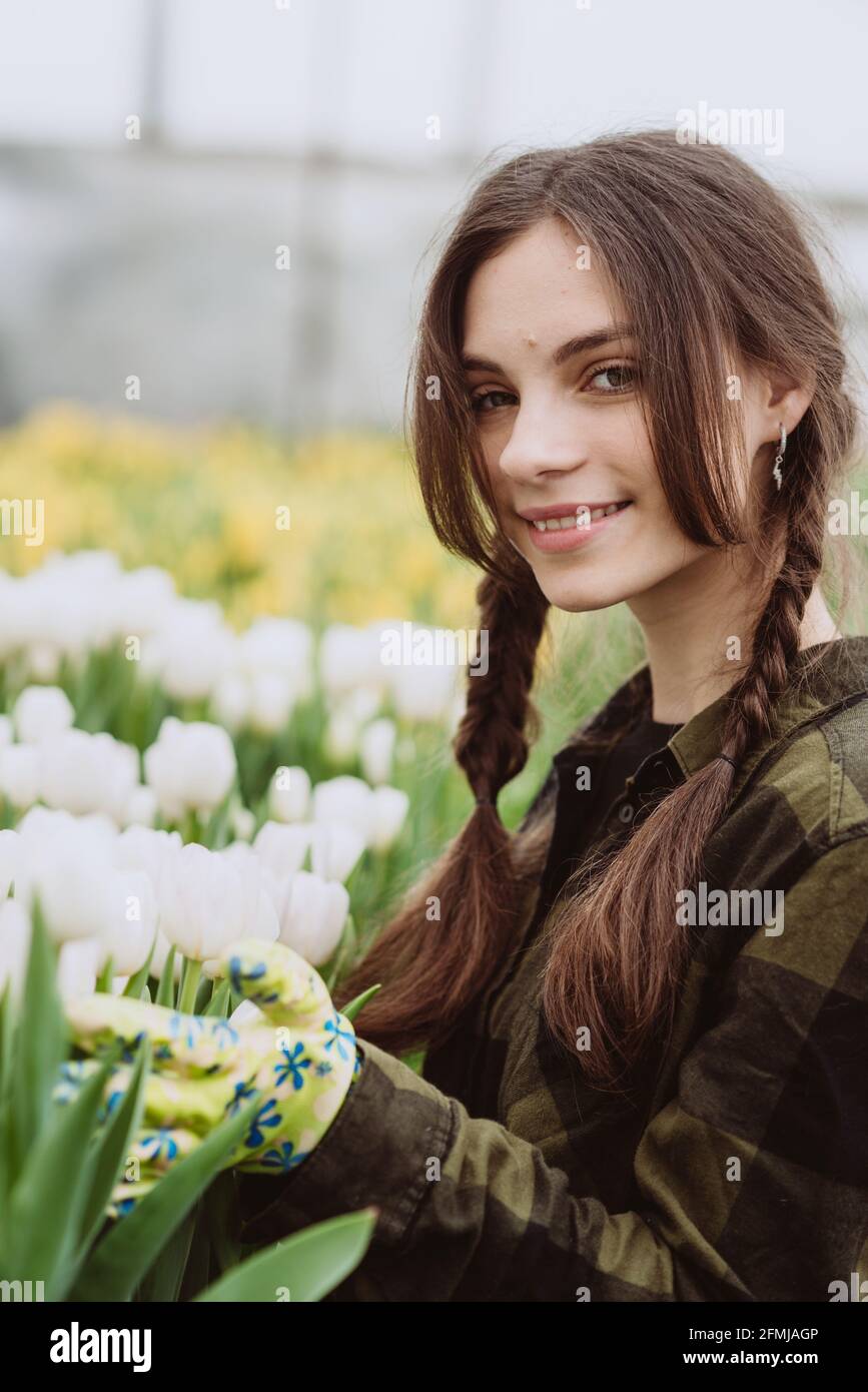 Junge Gärtnerin, die sich um Blumen aus Tulpen kümmert, die in einem Gewächshaus wachsen. Frühlingsblumen und Blumenzucht. Weicher, selektiver Fokus, Unschärfe-Effekt. Stockfoto