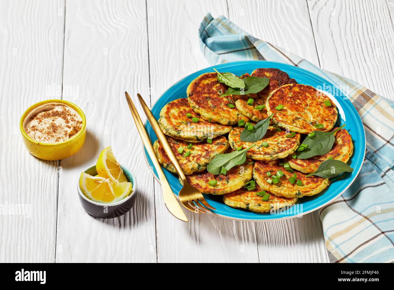 Kichererbsen Spinat Pfannkuchen auf einem blauen Teller auf einem weißen Holztisch mit Hummus in einer kleinen Schüssel Stockfoto