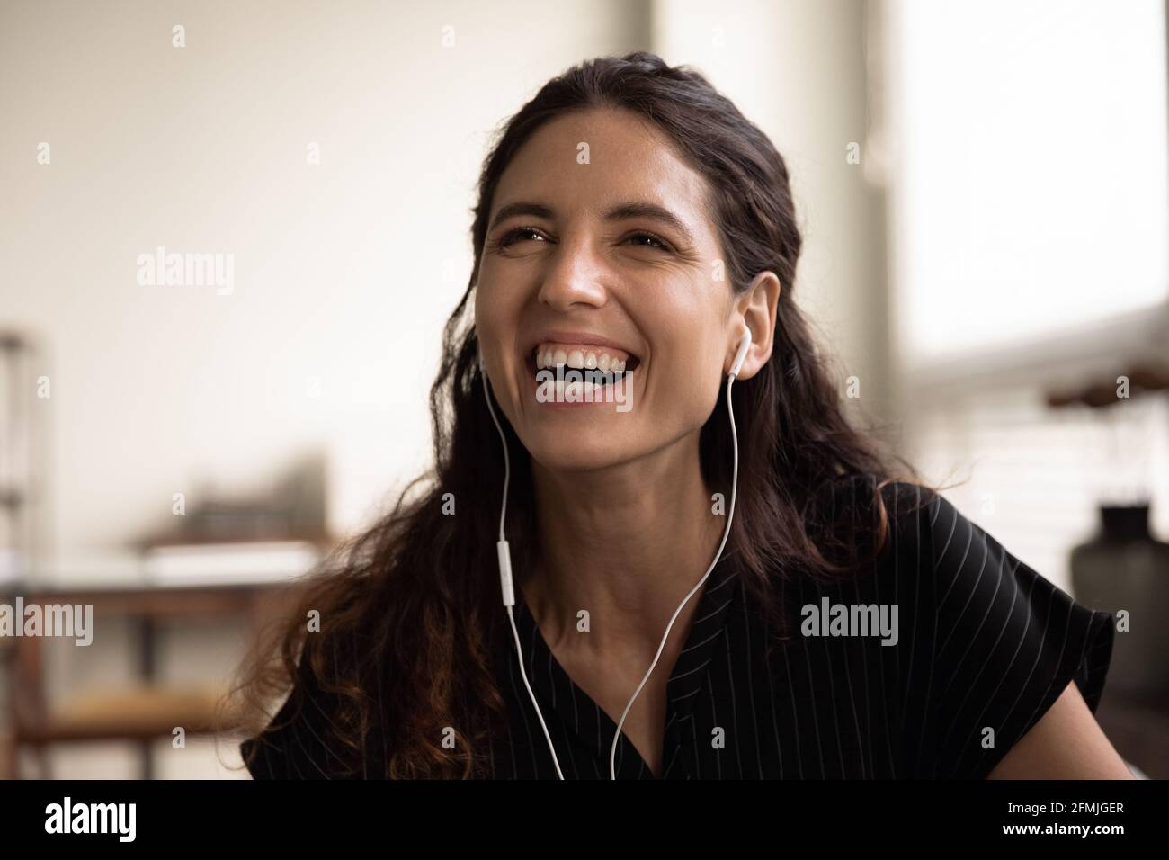 Kopfschuss einer überglücklich lachenden, tausendjährigen Latina-Frau mit kabelgebundenen Ohrhörern Stockfoto