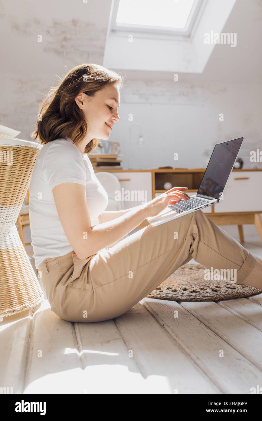 Das attraktive afroamerikanische Mädchen nutzt einen Laptop und lächelt beim Sitzen Der Boden Stockfoto