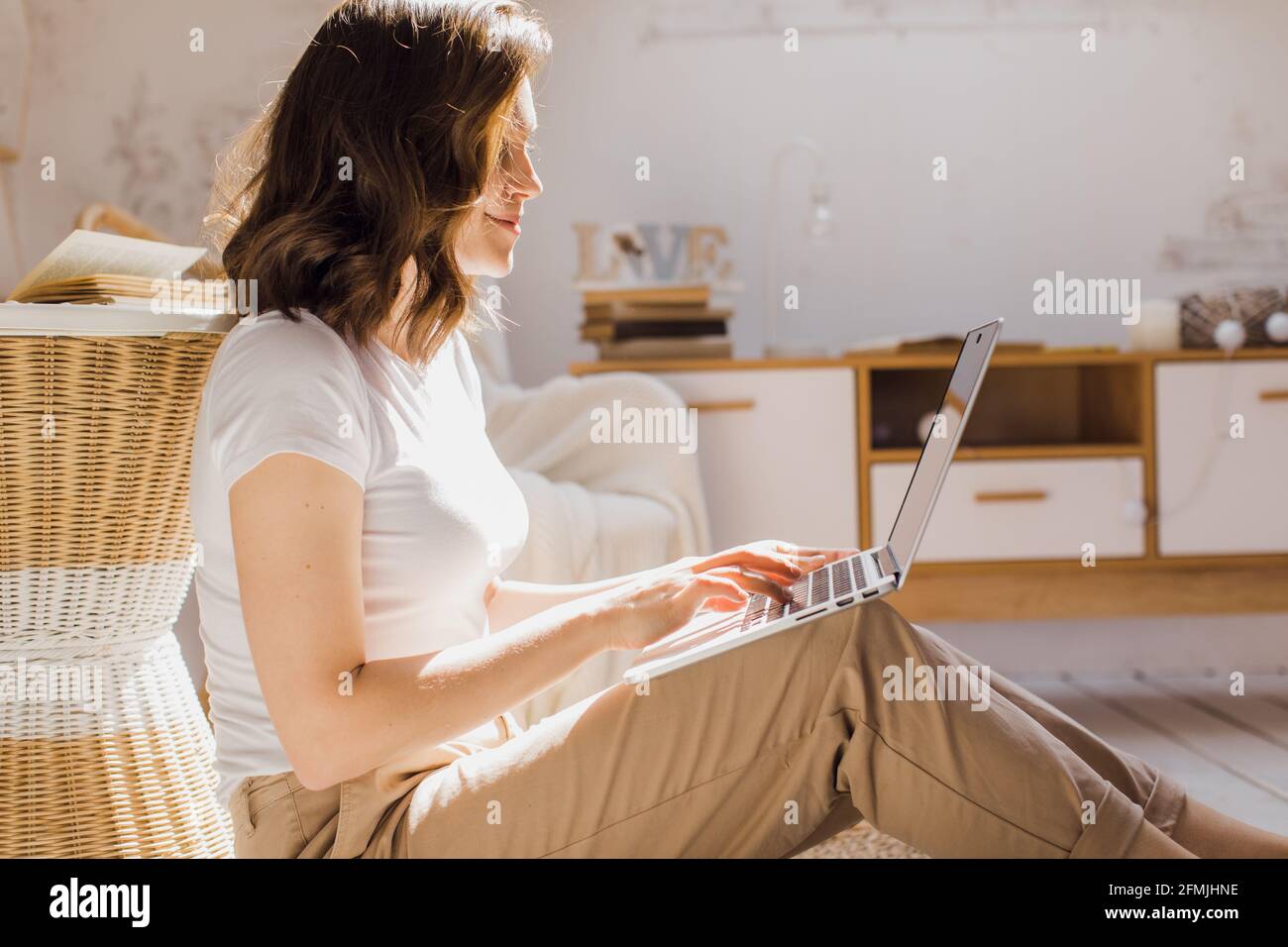 Das attraktive afroamerikanische Mädchen nutzt einen Laptop und lächelt beim Sitzen Der Boden Stockfoto