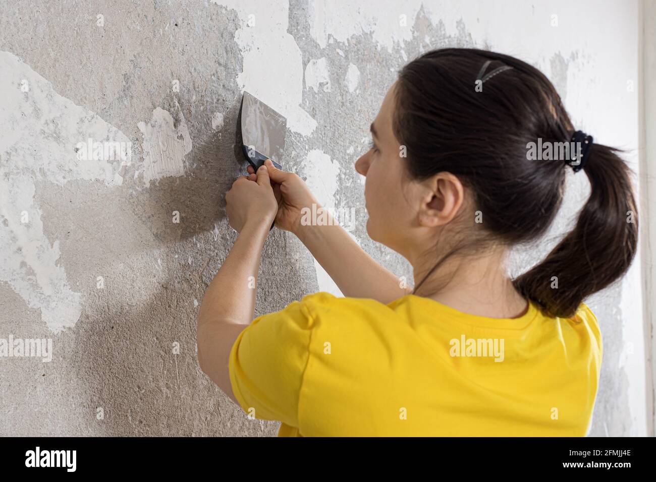 Die Werkstatt entfernt alte baumelnde Tapeten mit einem Spachtel von der Wand. Entfernen von Tapetenrückständen während der Reparatur. Stockfoto