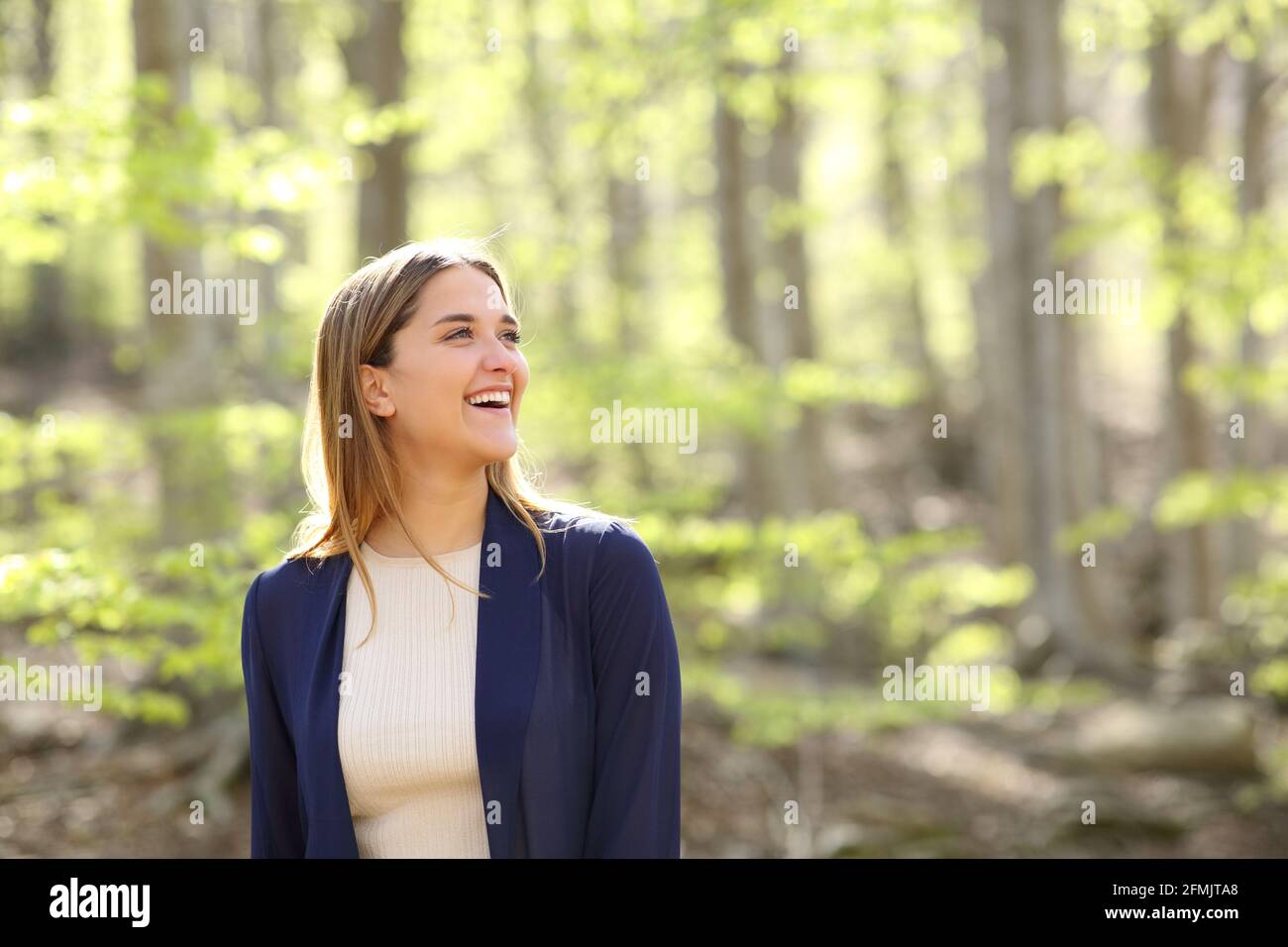 Glückliche Frau, die in einem wunderschönen Wald über die Aussicht nachdenkt und lacht Stockfoto