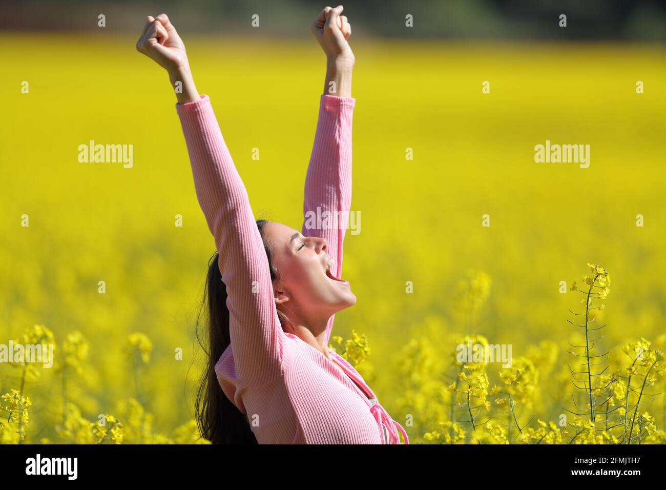 Seitenansicht Porträt einer aufgeregten Frau, die die Arme hochhebt Ein gelbes Feld im Frühling Stockfoto