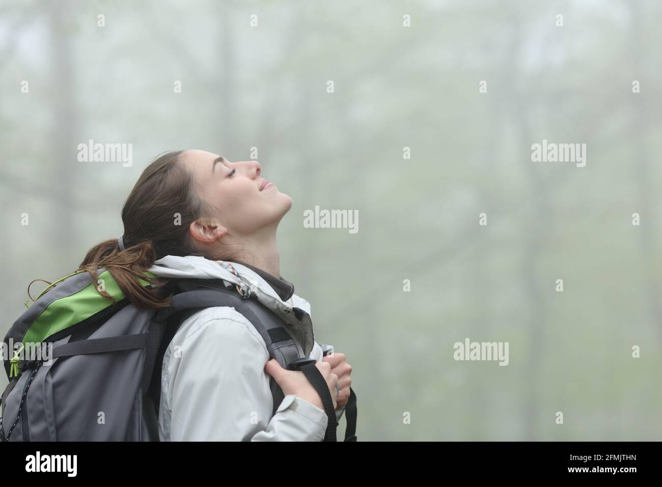Seitenansicht Porträt eines glücklichen Trekkers, der frische Luft atmet In einem nebligen Wald Stockfoto