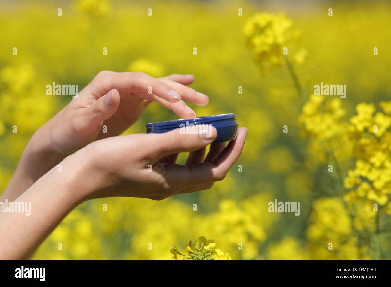 Nahaufnahme einer Frau mit der Hand, die ein Feuchtigkeitscreme-Glas hält Ein gelbes Feld im Frühling Stockfoto