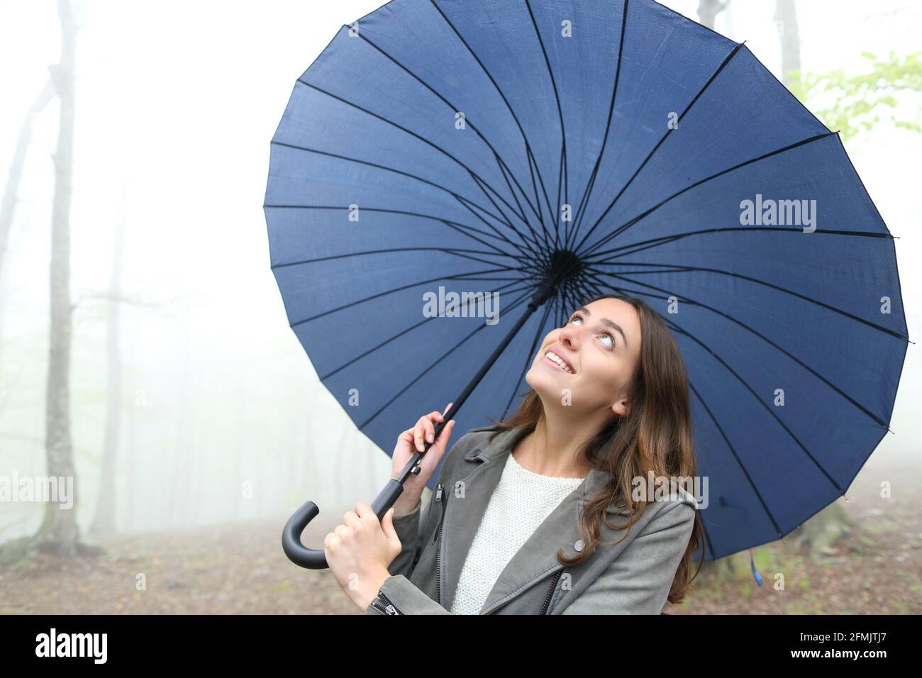 Glückliche Frau unter dem Regenschirm, die den Regen beim herkommen sah Ein nebliger Park Stockfoto