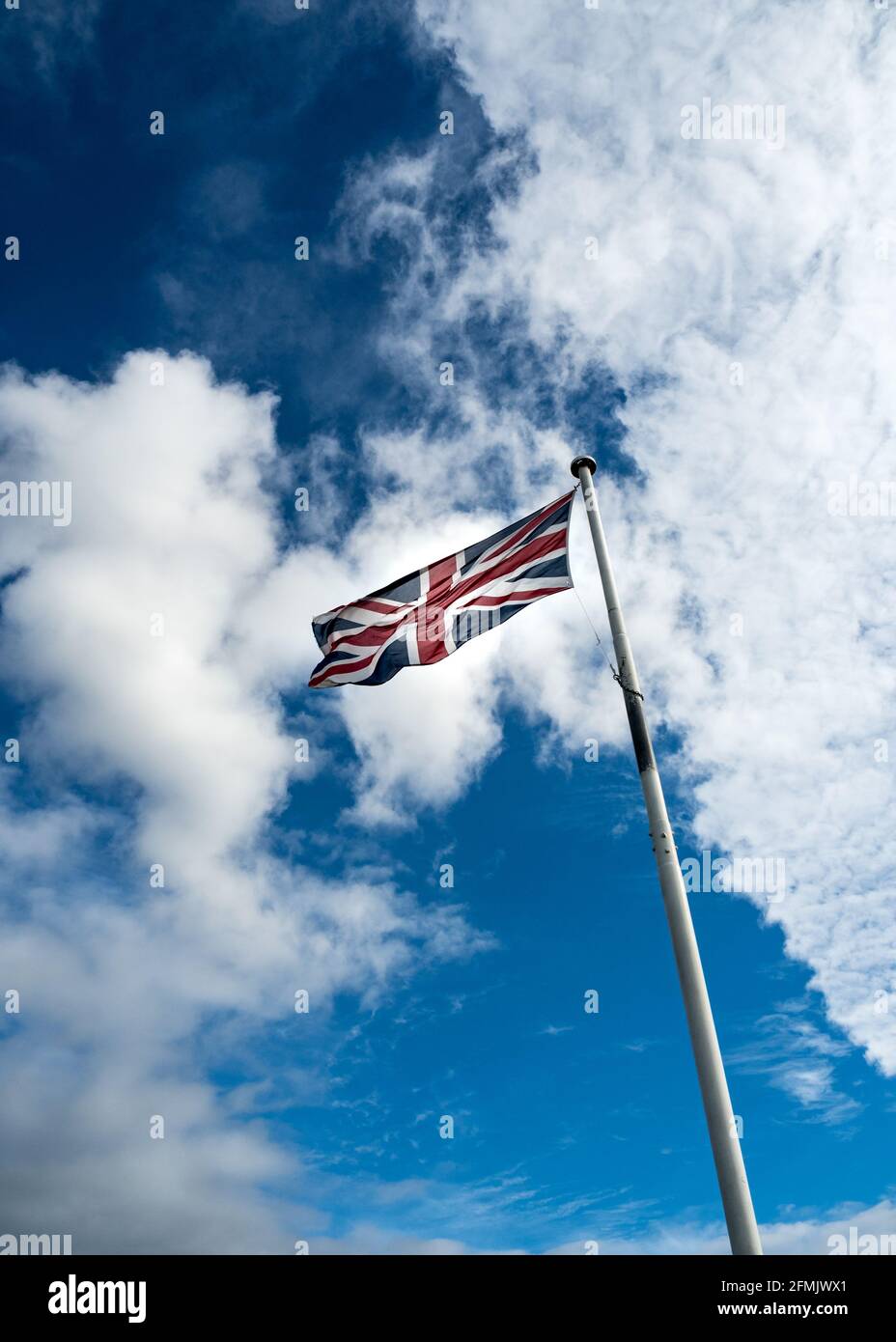 Die britische Flagge (Union Jack) auf einem Fahnenmast gegen einen blauen Himmel mit flauschigen weißen Wolken. Farbfoto. Stockfoto