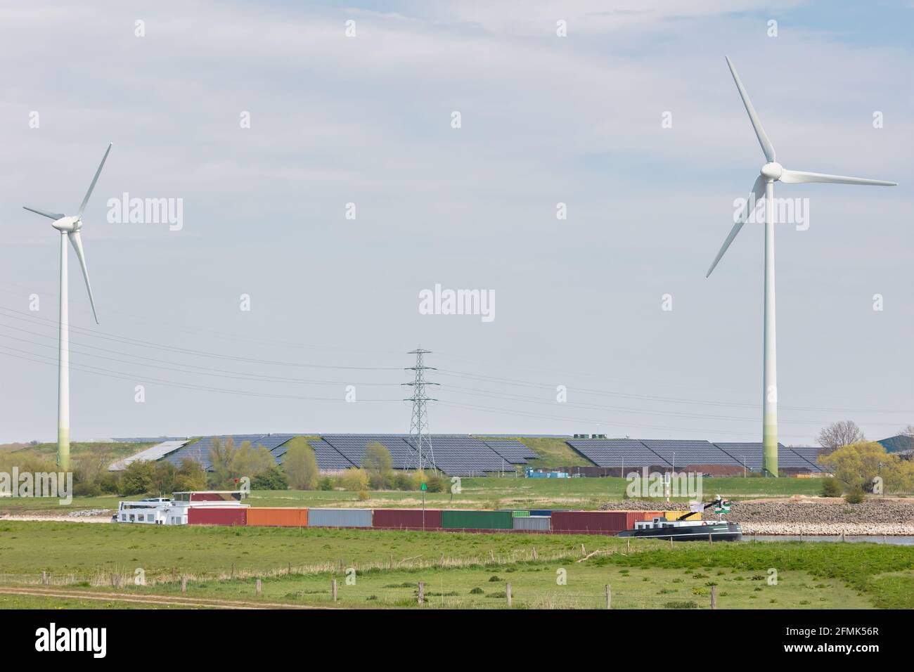 Vorbei Bulk-Containerschiff auf dem Fluss IJssel vor Einer großen Energieproduktionsanlage mit Windenergieanlagen und Sonnenkollektoren in den Niederlanden Stockfoto